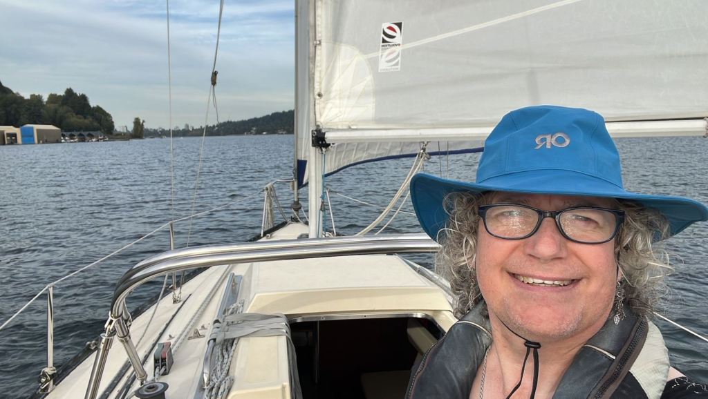 Sellfie: A person in a blue hat smiles from the deck of a sailboat. 