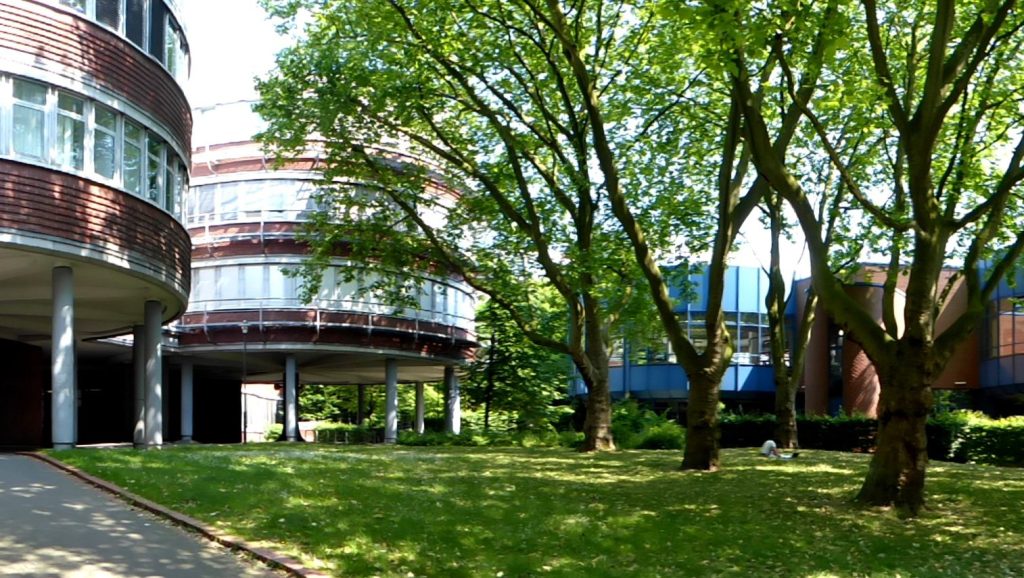 A sunny university campus featuring two circular brick buildings and trees. 